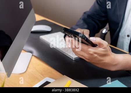 Visione parziale di un uomo d'affari concentrato che lavora in multitasking, tenendo un telefono all'orecchio mentre digita sulla tastiera di un computer Foto Stock