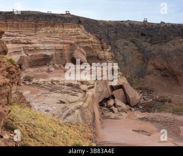 L'acqua a cascata scorre su rocce stratificate in un canyon, circondato da ripide scogliere e vegetazione sparsa. I cieli sovrastati migliorano lo scenario spettacolare Foto Stock