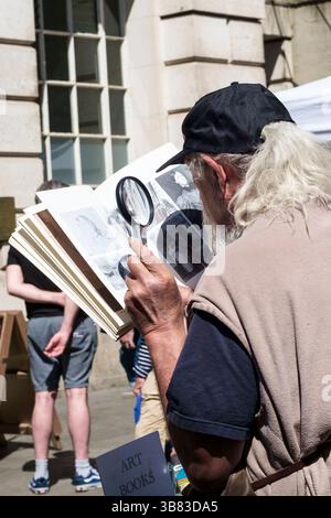 Mercato di sabato in Corn st nella città vecchia di Bristol Regno Unito uomo anziano con lente di ingrandimento che studia e vecchio libro Foto Stock