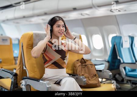 I turisti si godono la musica in aereo. Una giovane donna che si rilassa con le cuffie durante un volo. Foto Stock