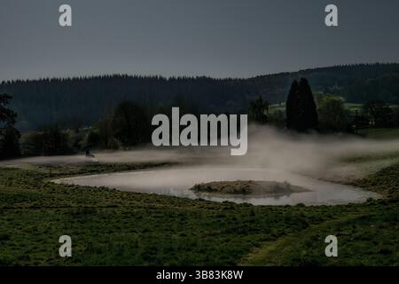 La nebbia è appesa in aria sopra uno stagno in una notte limpida e fredda, fotografata dalla luce della luna piena (Presteigne, Powys, Regno Unito) Foto Stock