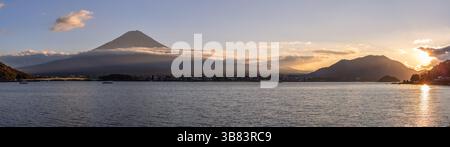 Vista panoramica del tramonto sul Lago Kawaguchi con il Monte Fuji sullo sfondo. La luce del sole dorata proietta lunghe ombre, illuminando le nuvole Foto Stock