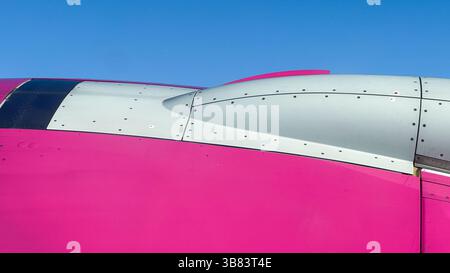 Vista ravvicinata della fusoliera rosa e bianca dell'aeroplano contro il cielo azzurro, evidenziando l'estetica moderna del design aeronautico e la precisione ingegneristica. Foto Stock