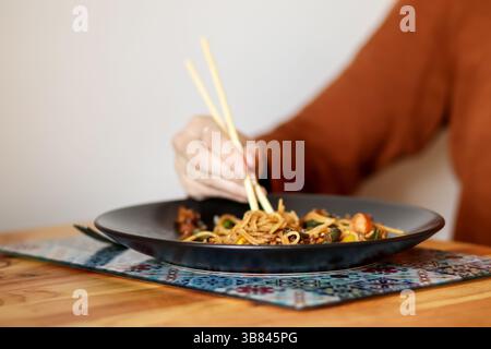 Donna che mangia spaghetti con le bacchette. Cucina asiatica. Primo piano di una donna che usa le bacchette per mangiare spaghetti. Delizioso cibo asiatico Foto Stock