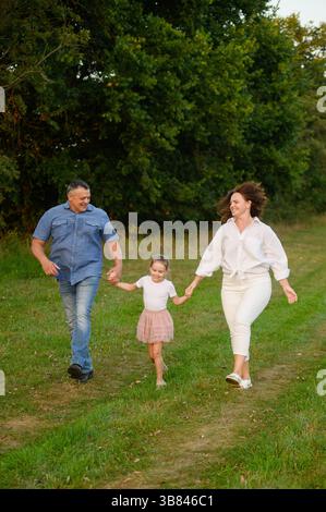 La famiglia si diverte a divertirsi nel parco, correre insieme, saltare per mano. Mamma, papa', figlia che si divertono insieme all'aperto, passano la settimana Foto Stock