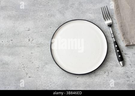 Piastra in ceramica vuota con forchetta su tavolo in pietra grigia, minimo posizionamento rustico del tavolo, vista dall'alto, spazio di copia Foto Stock