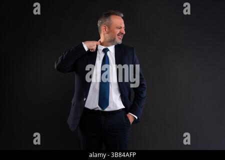 Uomo d'affari in tuta che tira il colletto della camicia, sembra scomodo e sudato. Concetto di calore, sollecitazione o pressione. Studio girato su backgroun scuro Foto Stock