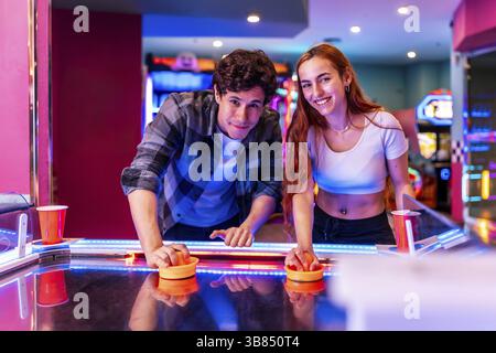 Amici multietnici che si divertono insieme giocando a hockey da tavolo in una colorata sala giochi Foto Stock