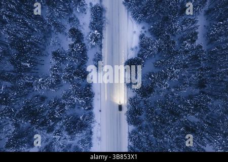 Vista aerea notturna della strada innevata nella pineta nella stagione invernale. Drone vista dall'alto verso il basso di neve strada invernale circondato pineta e abeti e. Foto Stock