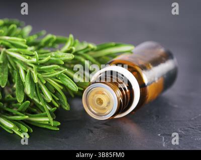 Olio essenziale di rosmarino in vetro scuro e bottiglia di rosmarino fresco su sfondo scuro con spazio di copia Foto Stock