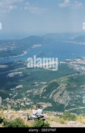 La sposa e lo sposo sono seduti su una panchina su una montagna sopra la Baia di Cattaro. Foto Stock