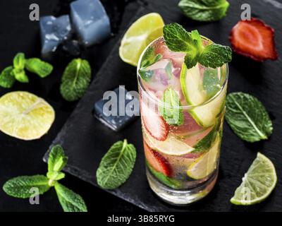 Limonata fresca con fragole, lime e menta su fondo in pietra scura. Bevanda estiva fredda alla fragola con menta e ghiaccio. Mojito di fragole in vetro e. Foto Stock