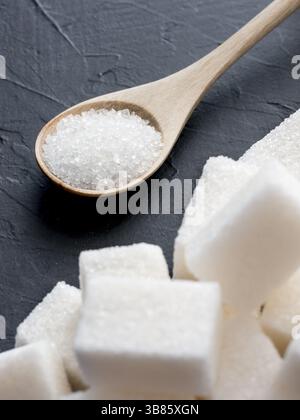 Fondo di cubetti di zucchero e zucchero in cucchiaio. Zucchero bianco su sfondo nero. Cubetti di zucchero e granulati in cucchiaio di legno Foto Stock