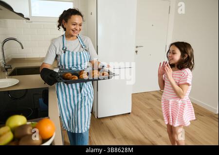 Una madre e una figlia che condividono un momento di gioia in una cucina luminosa mentre preparano croissant. L'atmosfera trasuda amore per la famiglia, cucina fatta in casa e un Foto Stock