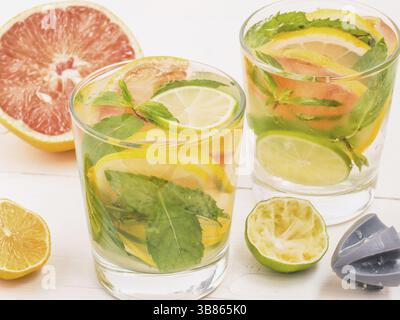 Freddo limonata fatta in casa con limone fresco, calce, pompelmo e menta da alesatore di limone. Bevanda estiva sul bianco sullo sfondo di legno Foto Stock