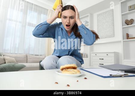 Giovane donna che guarda con disgusto gli scarafaggi su un tavolo bianco all'interno, vista ad angolo basso. Problema con i parassiti Foto Stock