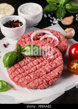 Vista ravvicinata di due cotolette di carne cruda per hamburger con verdure, spezie e basilico fresco. Preparare hamburger fatti in casa. Verticale Foto Stock
