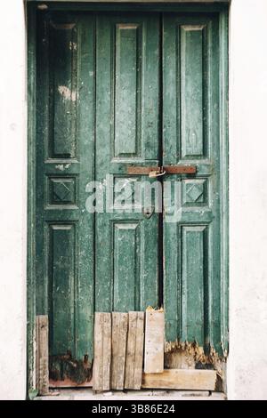 Primo piano di porte in legno verde fiabdo chiuse con un fondo rotto e tavole all'ingresso. Foto Stock