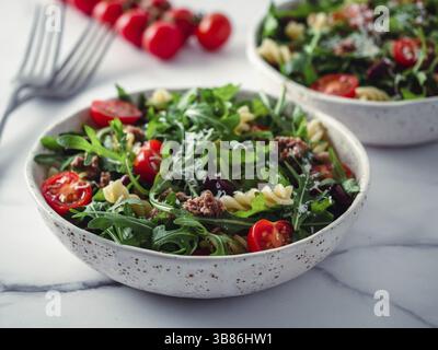 Insalata tiepida con tonno, rucola, pomodori, fagioli rossi, pasta. Idea e ricetta per un sano il pranzo o la cena. Due ciotole con insalate di caldo sul piano di marmo. Foto Stock