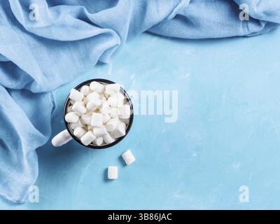 Marshmallows in cup on blue background with copyspace. Flat lay or top view. Background or texture of colorful mini marshmallows. Winter food backgrou Foto Stock