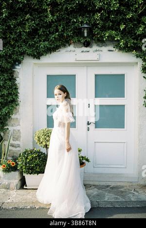 La sposa sorge di fronte all'entrata dell'edificio ricoperto di edera. Foto Stock