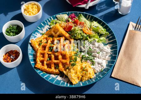 Waffle con uova strapazzate e formaggio fresco bianco serviti con verdure e verdure su un piatto splendidamente decorato, un set per la colazione, Foto Stock