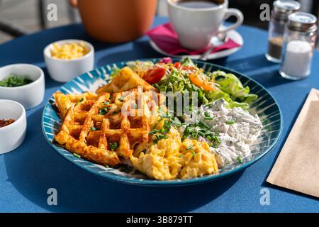 Waffle con uova strapazzate e formaggio fresco bianco serviti con verdure e verdure su un piatto splendidamente decorato, un set per la colazione, Foto Stock