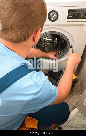 Tecnico che ripara la lavatrice utilizzando un cacciavite in bagno. Foto Stock