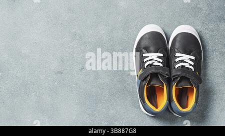 Un paio di nuove sneakers per bambini o adulti su sfondo in pietra grigia, vista dall'alto. Sneaker basse grigie e gialle o senape con spazio per le copie Foto Stock