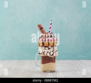 Il cioccolato e le ciambelle extreme frullato con marshmallow e altri dolci mason jar su grigio tavolo in legno e sfondo blu. Crazy freakshake su gr Foto Stock