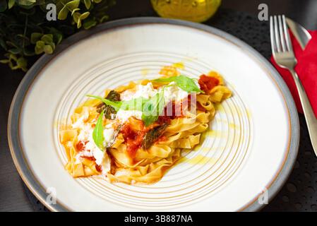 Tagliatelle tradizionali italiane condite con salsa di pomodoro, ricotta cremosa, basilico e olio d'oliva, servite su un piatto di ceramica. Foto Stock