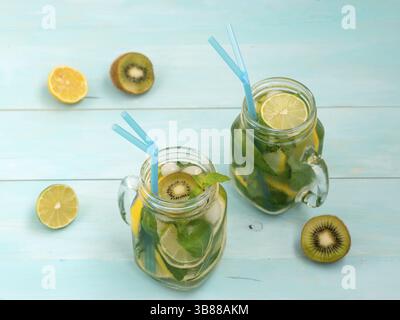 Freddo limonata fatta in casa con limone fresco, calce, kiwi e menta in mason jar. Bevanda estiva sul morbido blu sullo sfondo di legno Foto Stock