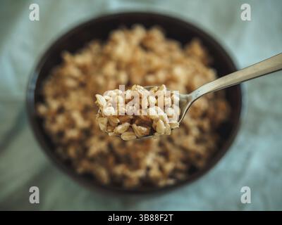 Il farro bollito in cucchiaio e non focalizzato nel recipiente. Il farro cotto semi in fuoco selettivo. Spazio di copia Foto Stock