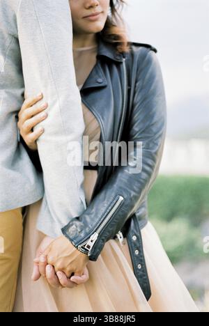 Sposa appoggiata sulla spalla dello sposo tenendo la mano. Ritagliato. Foto Stock