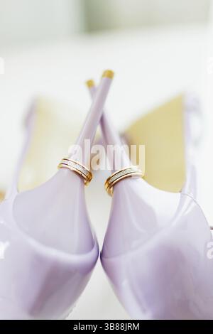 Anelli d'oro di nozze sui tacchi delle scarpe viola della sposa. Foto Stock