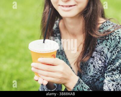 Donna tenere tazza di caffè sulla strada. Bicchiere di carta con caffè in mani all'aperto Foto Stock