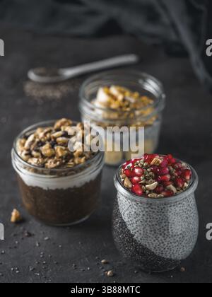 Set di budino di chia in diversi vasetti di vetro sul tavolo scuro. Assortimento di chia puding con frutta, noci e ingredienti diversi. Copia spazio per il testo. Su Foto Stock