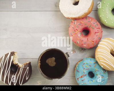 Vista dall'alto di ciambelle e caffè assortiti su sfondo in legno grigio con spazio per le copie. Ciambelle colorate e caffè con spazio imitabile. Varie ciambelle smaltate Foto Stock