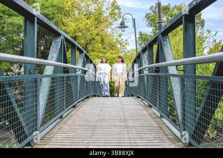 Due donne attraversano un pittoresco ponte in un parco tranquillo Foto Stock