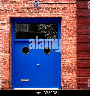 Le doppie porte blu vivo con finestre a oblò poste su una facciata in mattoni rossi creano un audace contrasto geometrico in un paesaggio urbano di Chicago Foto Stock