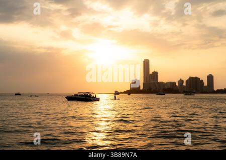 Tramonto sul moderno skyline di Cartagena, Colombia, visto dal mare con riflessi luminosi sull'acqua e sui cieli caldi. Foto Stock