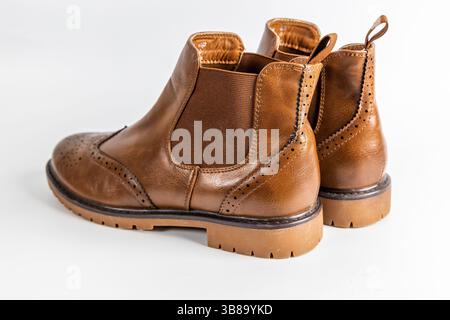 Un paio di stivali Chelsea marroni in pelle con dettagli in brogue e suola in gomma su sfondo bianco. Foto Stock