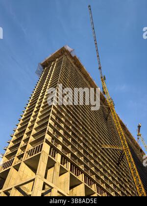 Alto edificio in costruzione con struttura in cemento e gru a torre, catturato da un angolo basso durante l'ora d'oro. Sviluppo industriale, non c'è gente Foto Stock