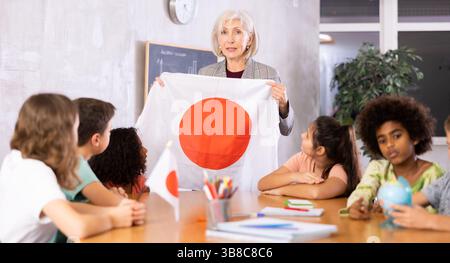 Insegnante donna che mostra la bandiera giapponese ai bambini in classe di geografia Foto Stock