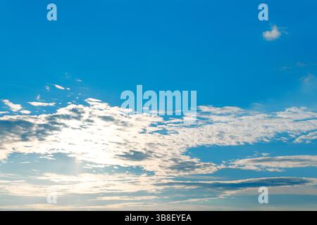 Cielo azzurro pieno di soffici nuvole bianche sparse, illuminate dalla luce soffusa del sole. La scena è calma ed espansiva, con una piccola nuvola di neve nelle vicinanze Foto Stock