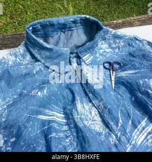 Camicia in denim senza finitura realizzata in lino, in attesa di cucitura all'aperto. Piccole forbici da taglio sulla camicetta per accorciare il battistrada. Foto Stock