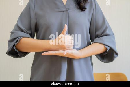 Foto ritagliata di una giovane donna sorda muta che usa il linguaggio dei segni su sfondo beige. Primo piano. Foto Stock