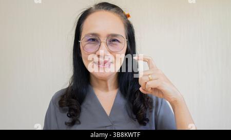 Persone adulte, stile di vita moderno, concetto di linguaggio del corpo. Primo piano di una donna asiatica matura che indossa gli occhiali con i capelli neri, guardando la fotocamera A. Foto Stock