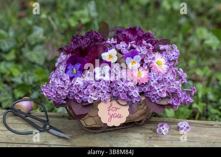 composizione floreale con fiori viola viola viola, tulipani, perennis bellis e fiori lilla in un cesto Foto Stock