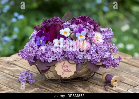 composizione floreale con fiori viola viola viola, tulipani, perennis bellis e fiori lilla in un cesto Foto Stock
